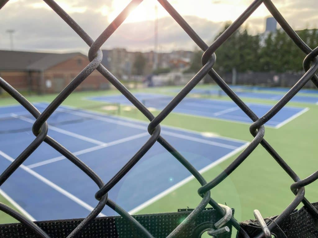 Courts de tennis vides vus à travers une clôture à mailles losangées