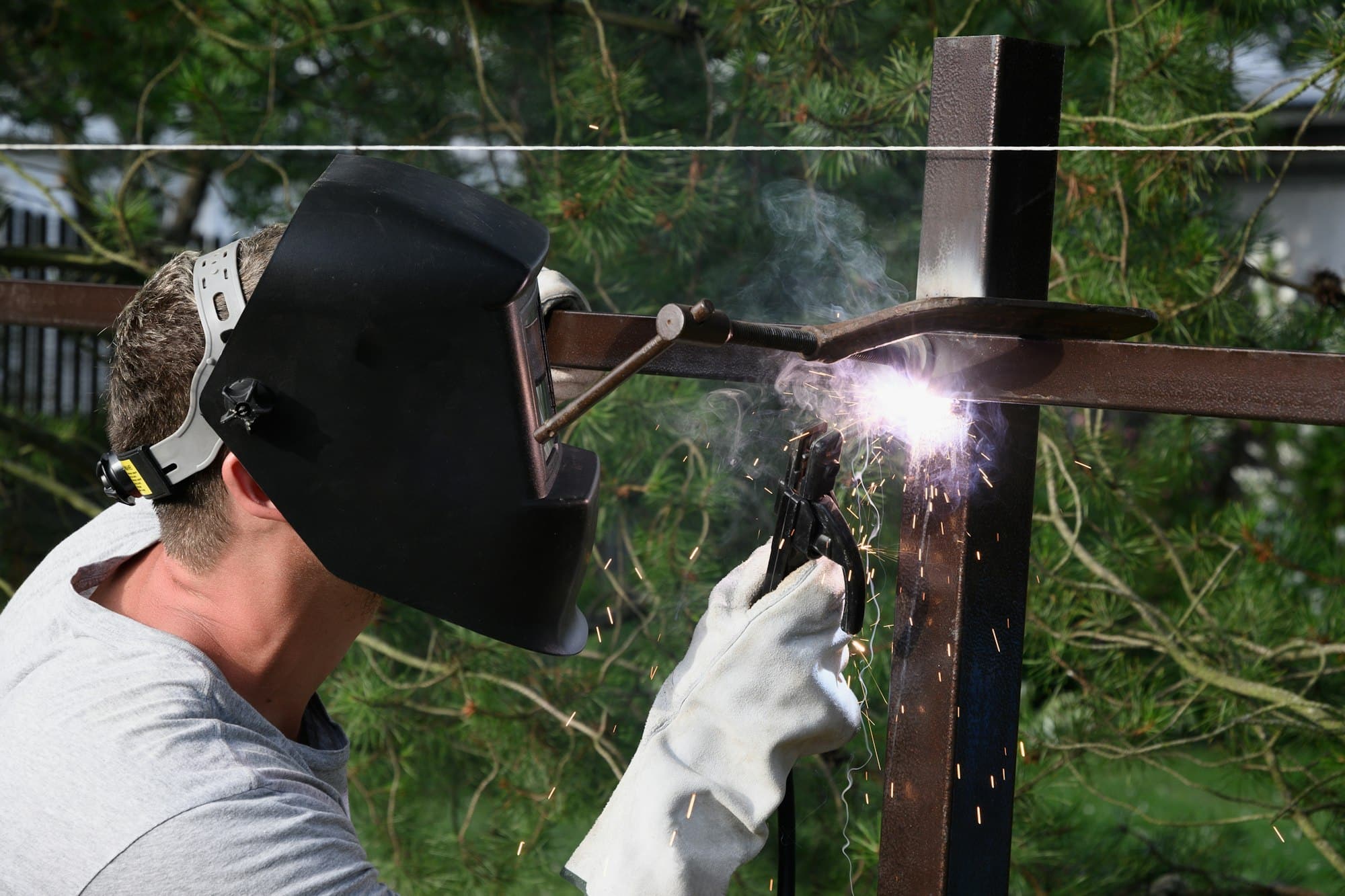 Um homem com uma máscara protetora e luvas especiais está construindo uma soldagem de cerca de metal.