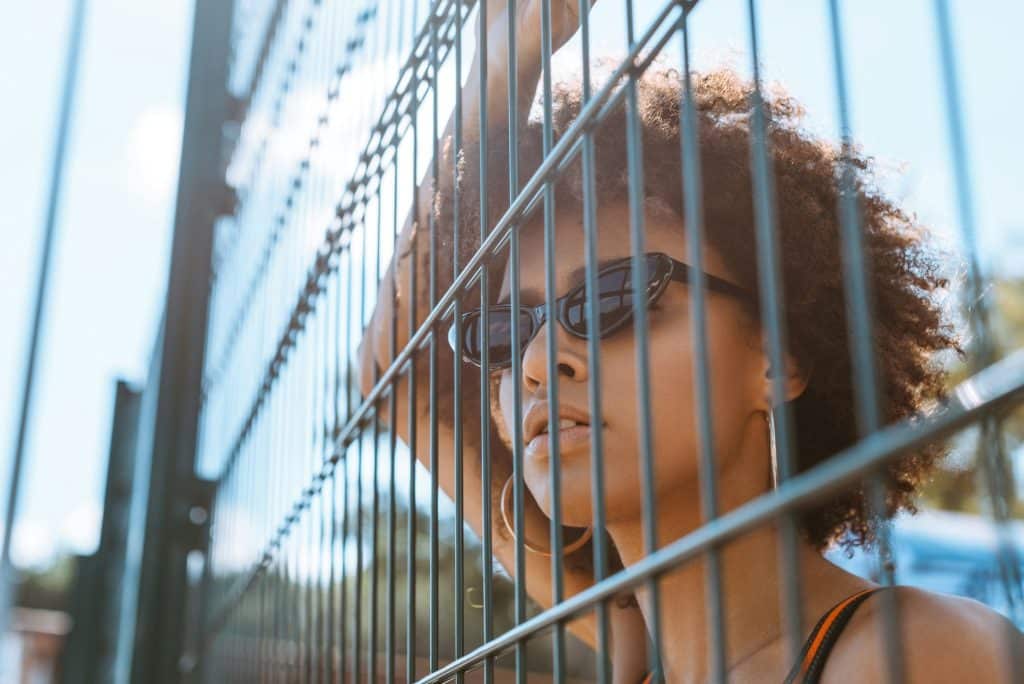 Joven afroamericana con gafas de sol posando detrás de vallas alambradas