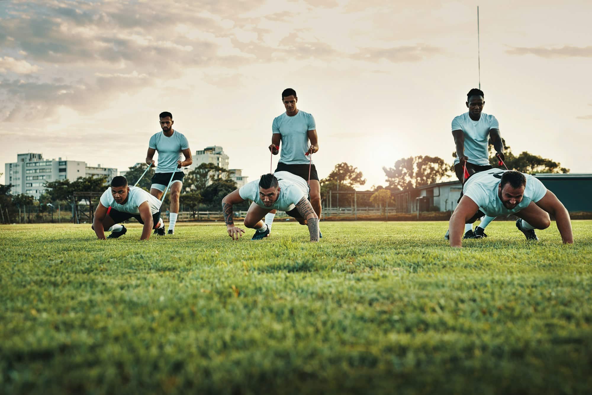 Ganzkörperaufnahme einer Gruppe junger Rugbyspieler, die tagsüber mit Bands auf dem Feld trainieren