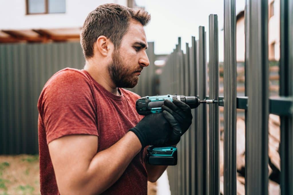 Construction worker using electrical screwdriver and mounting metal elements on fence