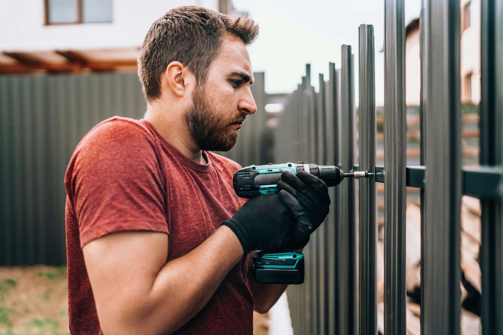 Construction worker using electrical screwdriver and mounting metal elements on fence